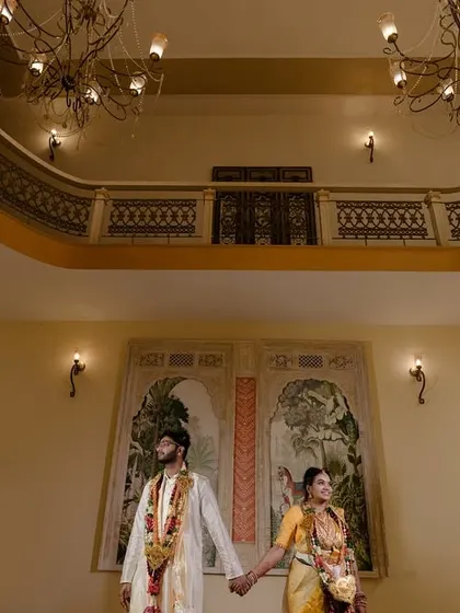 A wide shot capturing the grandeur of a South Indian wedding hall, with the couple engaged in the traditional rituals.