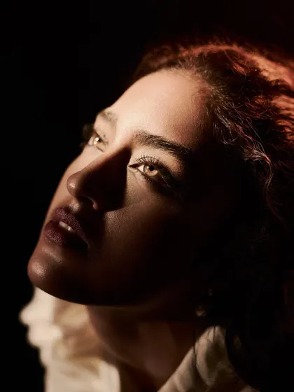 A dramatic, low-key beauty portrait. The light is coming from below and to the side, carving out the model's features and creating a sense of mystery and intensity.