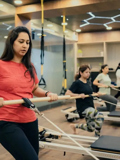 Clients use the wooden dowel for an arm and back exercise, focusing on posture and alignment. The entire class is engaged, showing the collective effort of a group session.