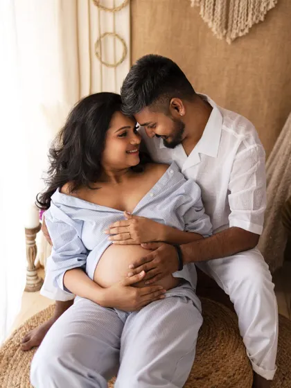 A romantic and intimate moment from a lifestyle maternity shoot. The couple shares a loving gaze, surrounded by the soft textures of the boho studio.