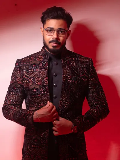 A groom's portrait that is all about style and confidence. The bold red background highlights the intricate details of his sherwani, creating a powerful, modern look.