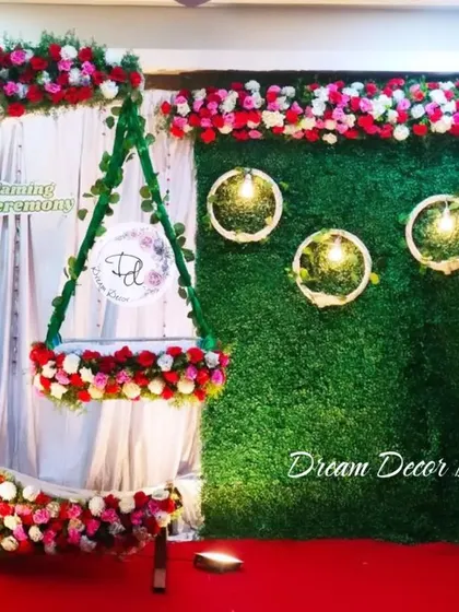 A popular design for naming ceremonies featuring a moon-shaped floral arch and a hanging cradle. This setup, done with artificial flowers, looks stunning against the green grass wall.