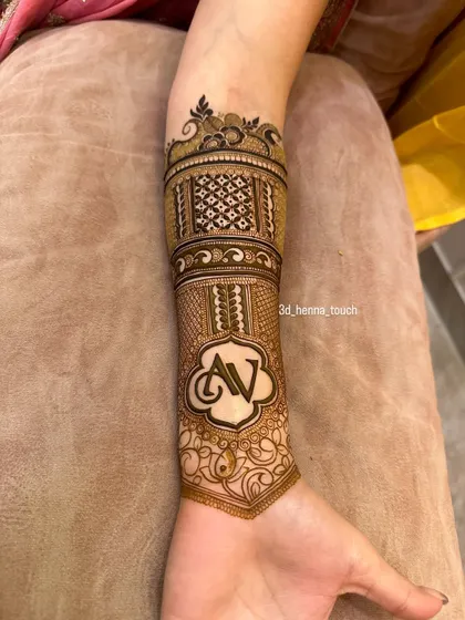 A personalized arm band featuring the initials 'AV' in a beautiful scalloped frame. This is a wonderful way to add a personal touch to your bridal mehndi.