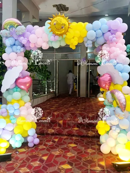 A full and fluffy pastel rainbow balloon arch with a smiling sun at its peak, making for a wonderfully happy party entrance.