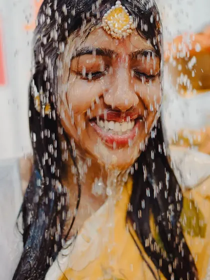 A close-up shot of the bride's face as she is showered with water during the Haldi ritual, her smile shining through.