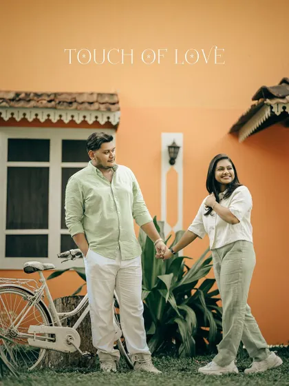 A candid shot of a couple walking hand-in-hand in front of a vibrant orange building, captioned "Touch of Love."