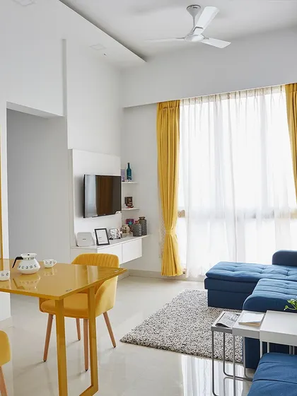 This living room combines a vibrant blue sofa with sunny yellow curtains and a matching foldable dining table, making it a cheerful and multifunctional space.