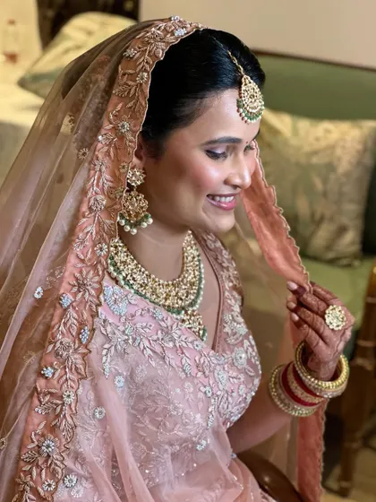 This bride is ready to say 'I do'. Her makeup is soft and radiant, and her hair is styled in a beautiful bun with fresh flowers, perfectly complementing her pastel lehenga.