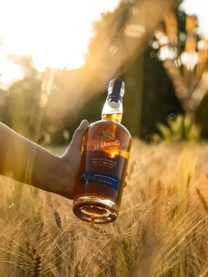 A beautifully backlit shot of the McDowell's bottle at sunset, with lens flare adding a magical, premium feel.