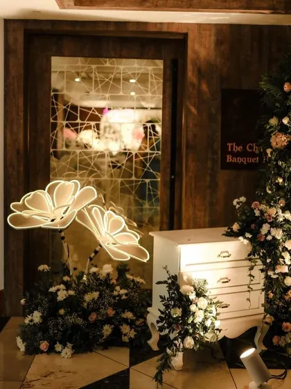 An elegant decor detail, featuring illuminated paper flowers and a vintage-style dresser at an event entrance.