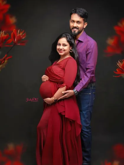 A bold and beautiful maternity portrait. The rich red gown stands out against the dark backdrop, framed by delicate red flowers for a dramatic effect.