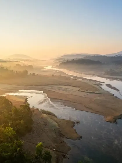 A misty sunrise over the Sharavathi River in the Western Ghats. The golden rays of the sun cut through the fog, creating a magical atmosphere.