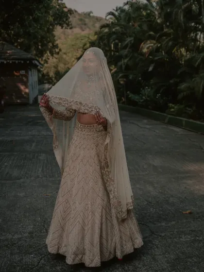 A bride draped in an elegant white lehenga, her face partially covered by a delicate veil. This portrait is full of grace and mystery.