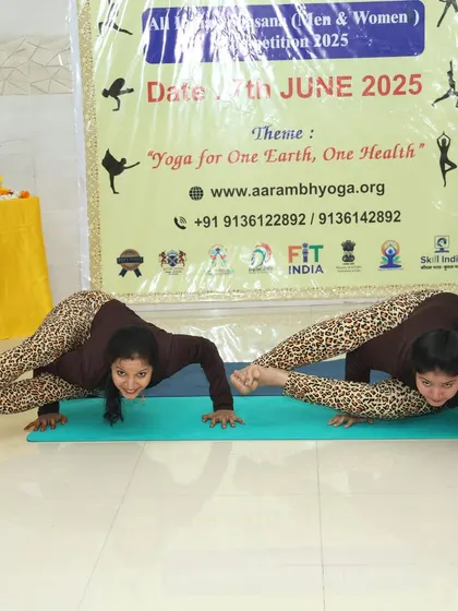 Two participants hold a synchronized arm balance pose, Mayurasana (Peacock Pose), showcasing immense core and arm strength.