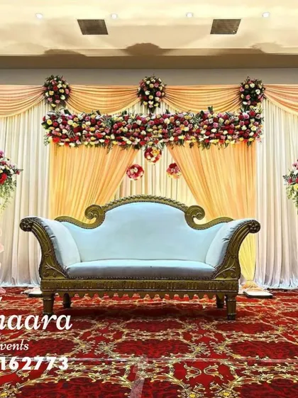 An elegant engagement stage with a classic color palette. The peach and cream drapery is complemented by rich red and white floral bouquets on tall stands, creating a sophisticated look.