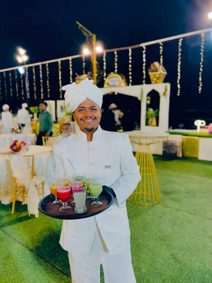 A server in a traditional white uniform offers a tray of colorful, freshly pressed juices to guests.