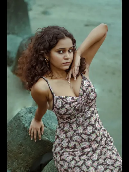 A direct and engaging portrait. The model is leaning against the rocks, which adds a rugged texture that contrasts nicely with the soft floral pattern of the dress.