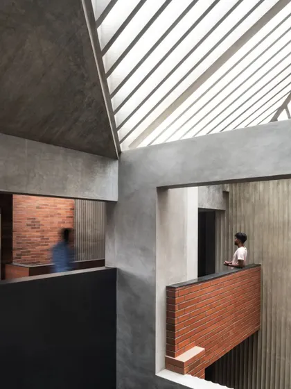 The central atrium of the Brick House, where light from a slatted skylight filters down, illuminating the different levels and highlighting the interplay of brick and concrete.