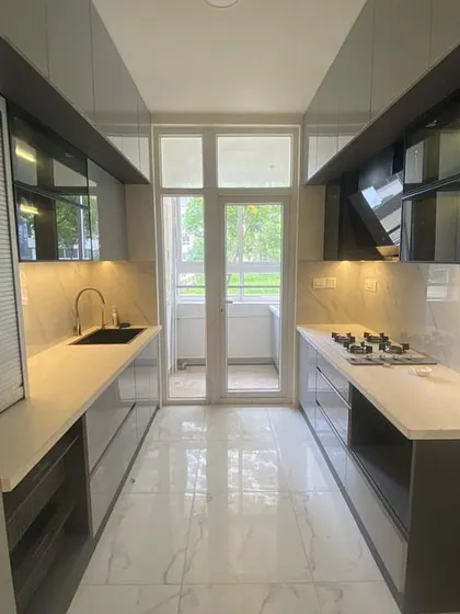 We designed this sleek galley kitchen to maximize space and functionality. It features handleless cabinets in a cool grey tone, a durable white quartz countertop, and integrated under-cabinet lighting for a clean, modern aesthetic that makes cooking a pleasure.