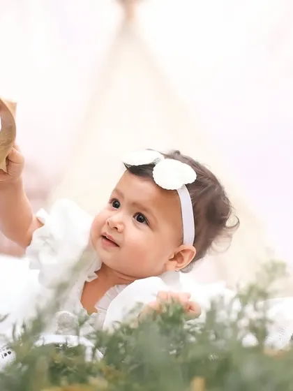 A moment of pure curiosity as a little girl in a white dress examines a leaf. The soft, bright lighting gives this outdoor portrait an angelic feel.