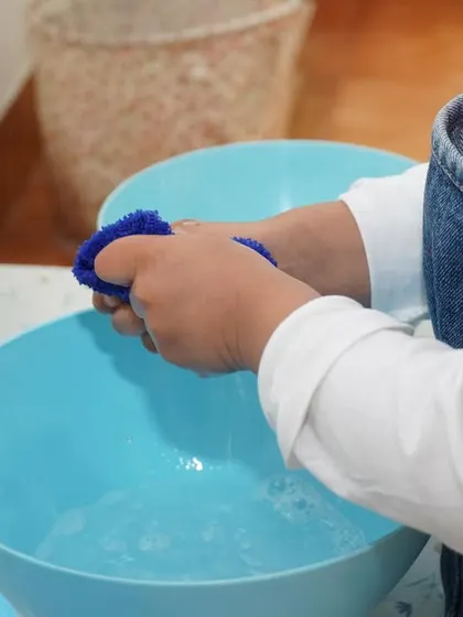 A close-up of a child's hands washing with a sponge. Water activities are always a favorite, and they are excellent for developing sensorial awareness and fine motor skills.