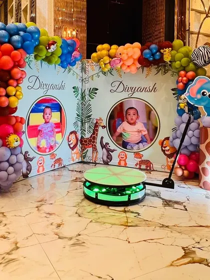 A jungle-themed photo corner with personalized backdrops for each twin, surrounded by animal characters and colorful balloons.
