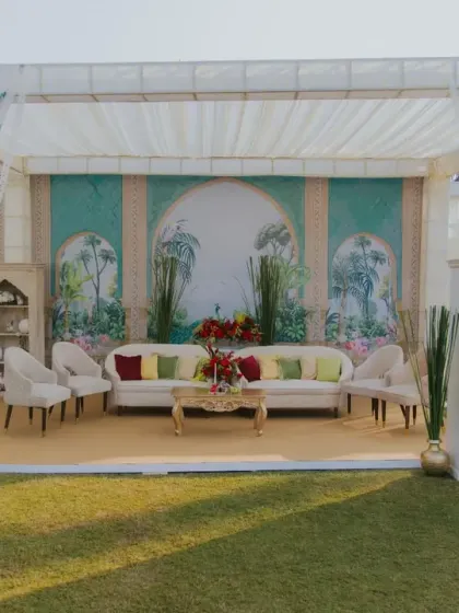A serene lounge area at the wedding ceremony, featuring a backdrop with hand-painted illustrations. We create these comfortable and aesthetically pleasing spaces for guests to relax and mingle.