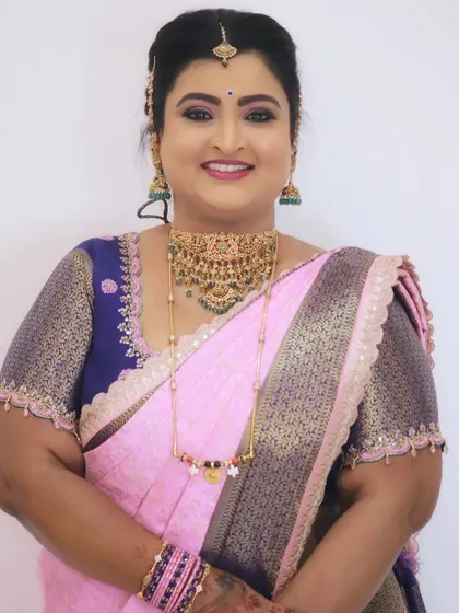 A smiling portrait showcasing a complete traditional look, with flawless makeup, a classic hair updo, and beautiful temple jewelry.