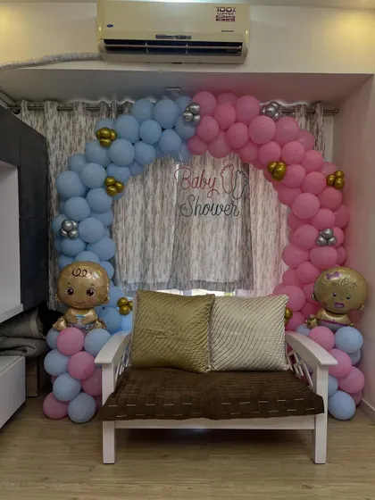A classic "He or She" themed baby shower decoration. This setup features a beautiful balloon arch with distinct pink and blue sections, accented with baby-shaped foil balloons to create a perfect photo spot for the parents-to-be.