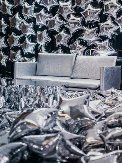 A photo booth moment from 'The Melting Disco Ball', featuring a wall of silver star balloons and a floor covered in confetti. Every corner of this event was designed to be an immersive, high-glam photo opportunity.