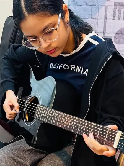 Focus and precision are key. This student is deep in concentration, practicing her fingerpicking technique on an acoustic guitar, an essential skill for any aspiring guitarist.
