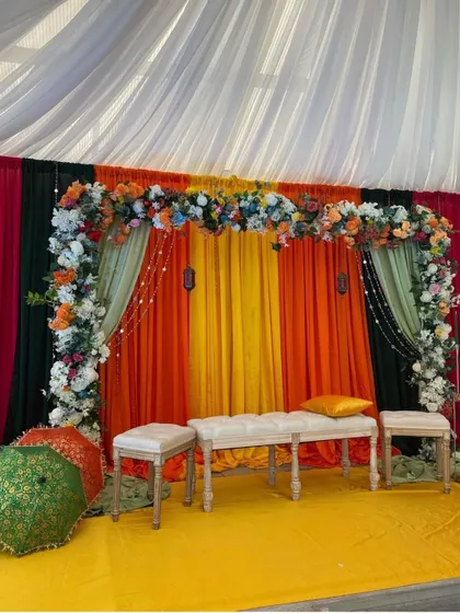 A colorful stage setup perfect for a Sangeet or Mehendi. The multi-colored drapes and floral arch create a festive and lively backdrop.