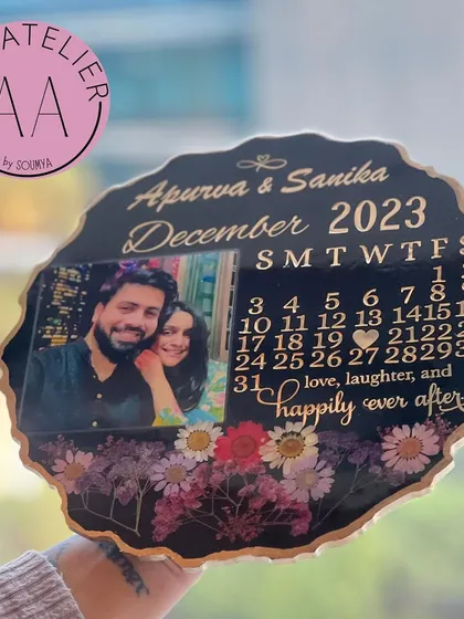 A close-up of the black resin anniversary calendar, held against a bright window to show the beautiful details of the preserved flowers and gold lettering.