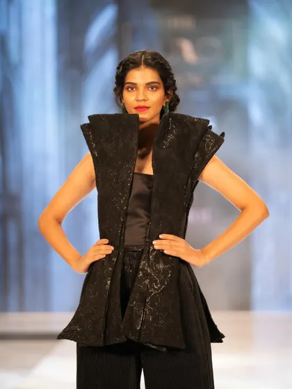 A strong, structured look from The Luxo Show. The makeup features a classic red lip and clean skin, allowing the architectural design of the outfit to stand out.
