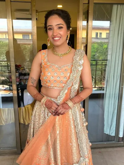 A full-length shot of the groom's sister in her beautiful peach lehenga. The makeup is soft and warm to complement her outfit.
