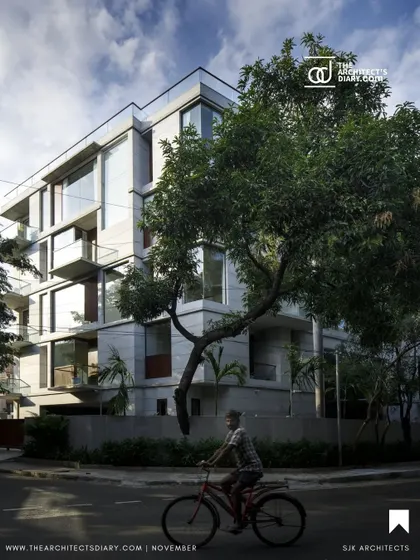 The Boat Club Apartments viewed from the street, nestled amongst mature trees. The design aims to be a respectful addition to the neighborhood, balancing modern aesthetics with a connection to its natural context.