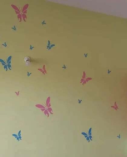 A playful children's room wall with pink and blue butterfly stencils scattered across a soft yellow-green background.