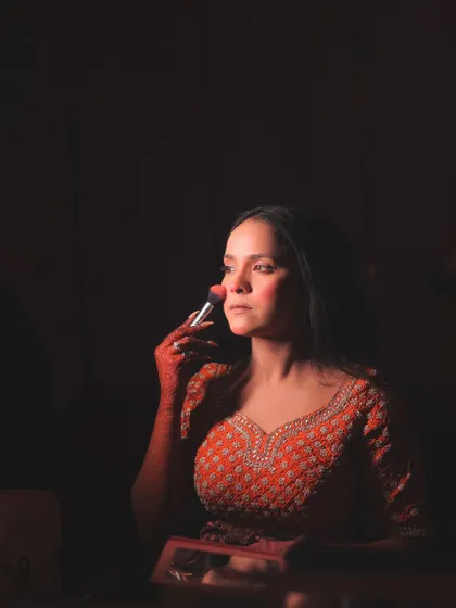 A candid moment of the bride applying her own makeup, captured with dramatic, low-key lighting for an intimate feel.