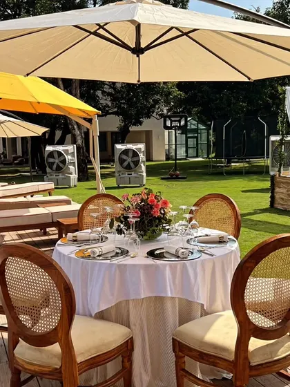 An elegant round table setup for a brunch, with classic rattan chairs and a simple floral centerpiece under a large patio umbrella.