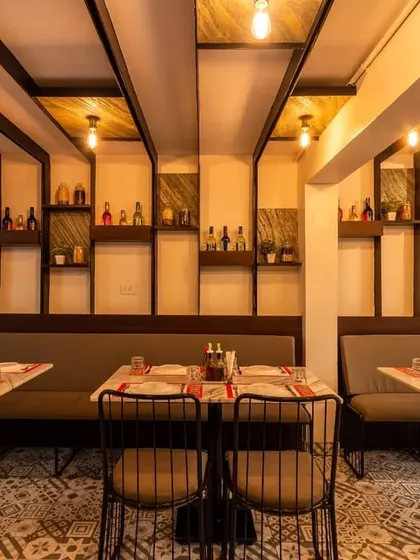 A cozy dining nook designed with long booth seating against a wall featuring decorative shelving and vertical wood-finished panels. The exposed Edison bulbs hanging from the ceiling add a warm, vintage touch to this intimate area.