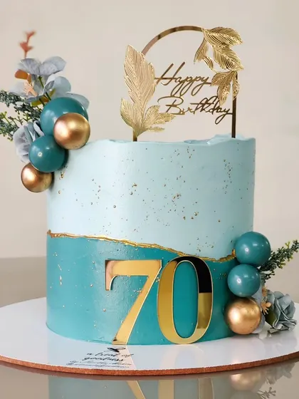 Celebrating a 70th birthday in style with this two-tone teal cake. The design is modern and clean, with a large acrylic number, gold-dusted edges, and a simple arrangement of decorative spheres.