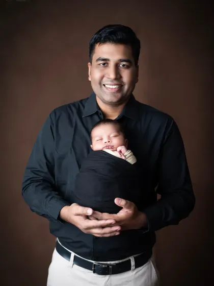 A happy father holds his newborn son, both dressed in black for a timeless and classic portrait.