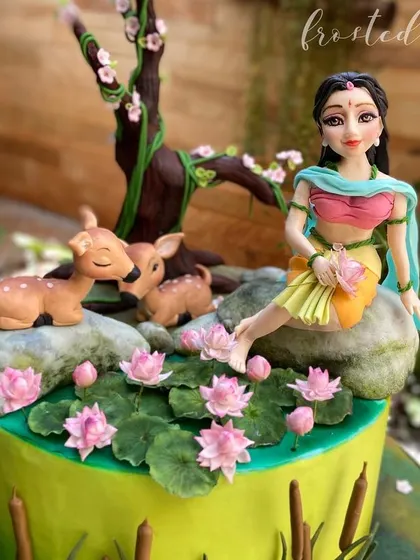 This cake, inspired by the story of Shakuntala, won 3rd place at Cakeology. It features a serene scene with a hand-sculpted figurine, gentle fawns, and delicate sugar lotuses.