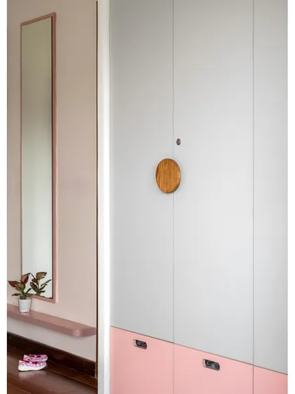 The daughter's room in 'Vasudhalayah' features a sleek wardrobe with a unique circular wooden handle, set against a soft pink and grey color-blocked design.