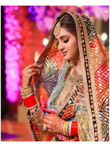 A stunning portrait of the bride in her multi-colored Rimple and Harpreet lehenga. The side profile highlights the intricate details of her dupatta and her elegant posture.