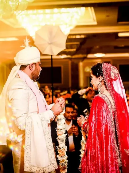 A wide shot of the Varmala ceremony, showing the couple surrounded by their guests. The warm, golden light creates a celebratory and magical atmosphere.
