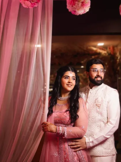 A candid shot of the couple sharing a happy moment during their engagement ceremony. The soft pink decor and sheer curtains create a dreamy and romantic atmosphere.