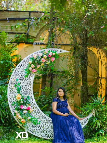 A dreamy solo portrait of the mother-to-be sitting on a floral crescent moon prop in a garden.