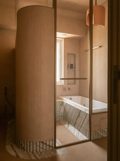 A view into the bathtub area, which is enclosed by a curved, micro-concrete partition, creating a private and serene bathing nook.