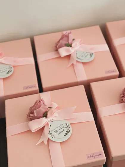 The final touch on our bridesmaid proposal boxes. Each pink box is tied with a ribbon and a custom tag asking, "Will you be my bridesmaid?", making the moment truly special.
